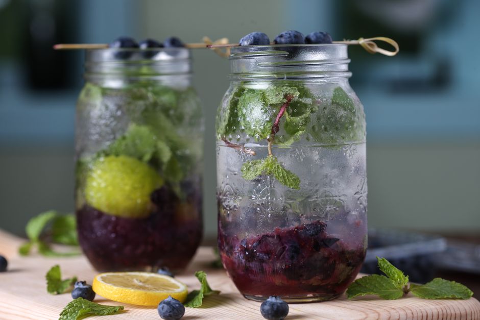 Close-up of refreshing blueberry mint drinks in glass jars with lemon slices on a wooden board.
