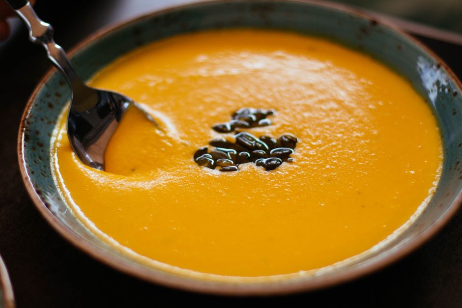 A bowl of roasted butternut squash soup with a cream swirl and seeds