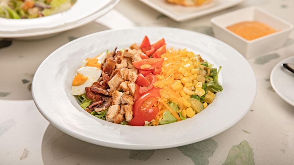 A loaded Cobb salad with rows of chicken, bacon, egg, and avocado