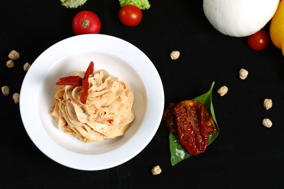 Delicious creamy sun-dried tomato dip in a bowl with fresh ingredients on display.