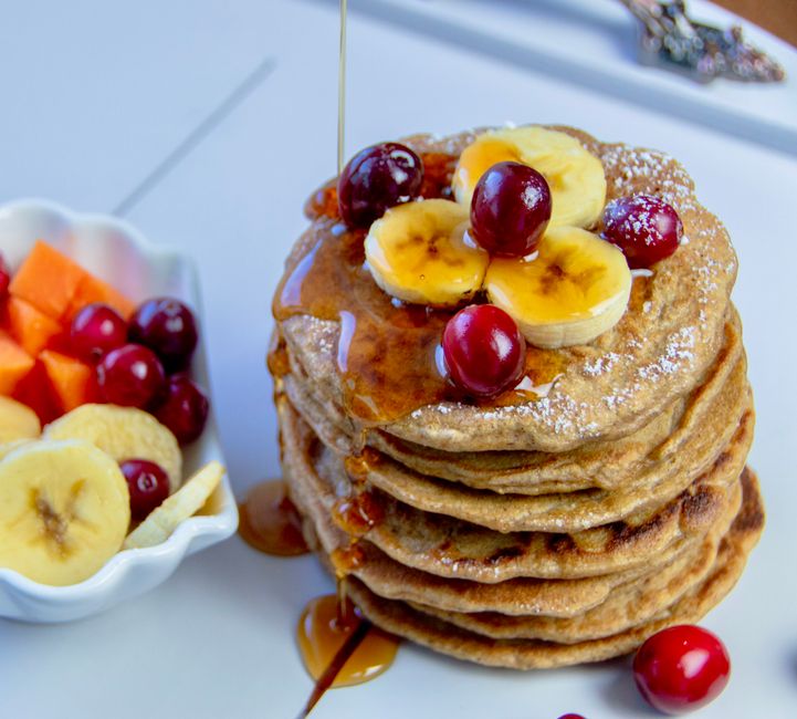 Stack of pancakes topped with bananas and cherries, drizzled with syrup, perfect for breakfast.