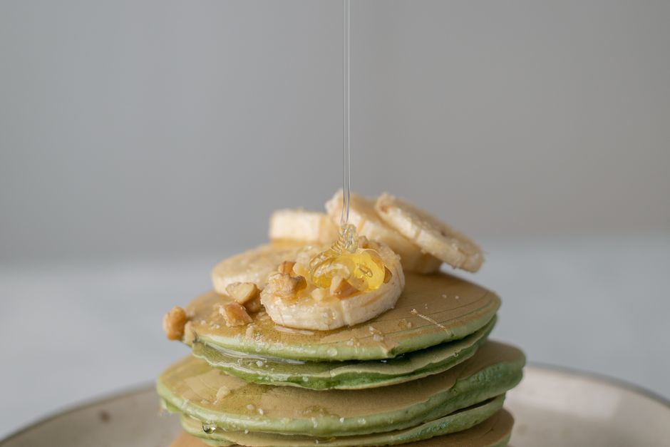 A tall stack of banana pancakes with maple syrup and banana slices