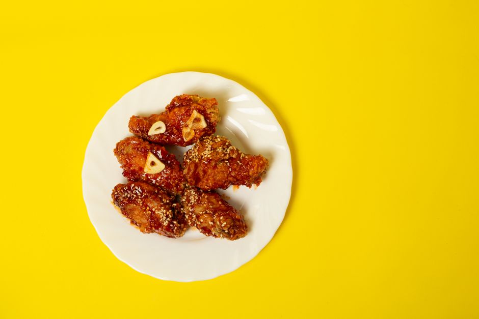 Delicious crispy fried chicken wings with garlic and sesame seeds on a vibrant yellow background.