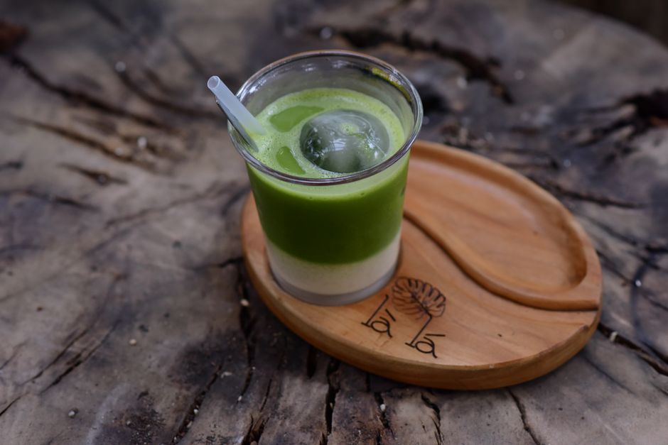 A layered iced matcha latte in a tall glass with a straw