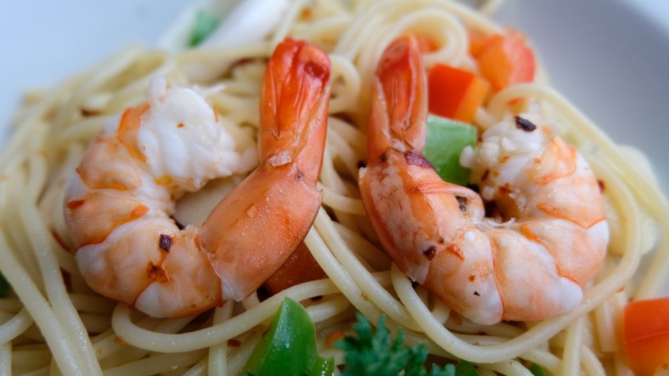 Tasty shrimp pasta dish garnished with colorful vegetables in close-up view.
