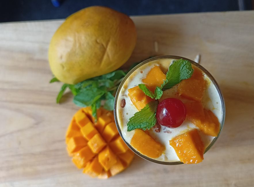 Refreshing mango lassi adorned with fresh mint and cherry, perfect summer drink.