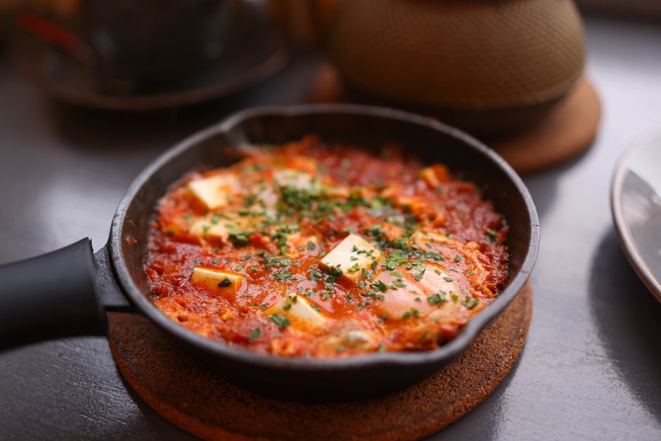 shakshuka eggs poached in tomato sauce in cast iron pan with fresh herbs
