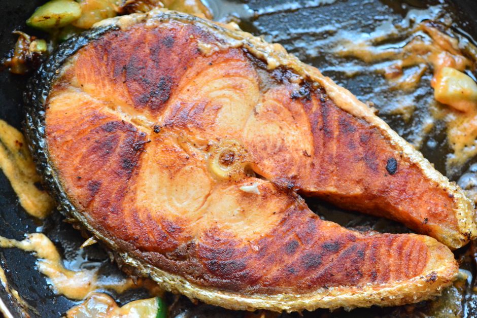 A close-up of a deliciously fried salmon steak sizzling in its juices in a pan.
