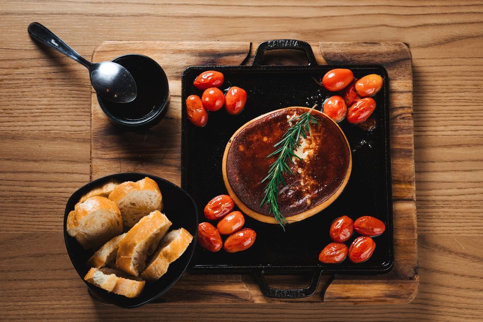 Block of feta cheese surrounded by roasted cherry tomatoes in a baking dish