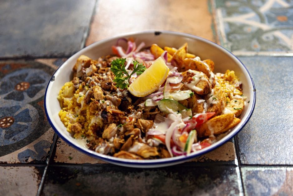 A vibrant chicken shawarma platter with rice, vegetables, and a slice of lemon, presented on a colorful mosaic table.