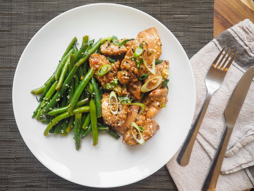 Sticky orange chicken in a skillet garnished with sesame seeds and green onion