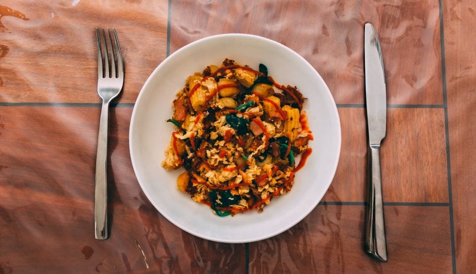 A vibrant vegetarian stir fry with colorful veggies served on a white plate with cutlery.