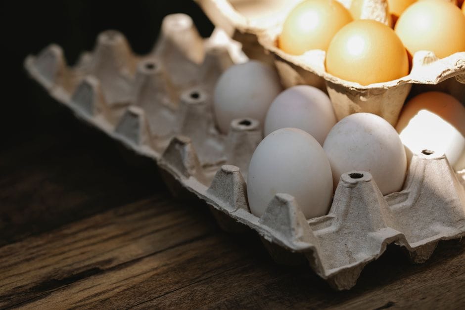 From above of fresh chicken eggs in carton container placed on wooden table in kitchen