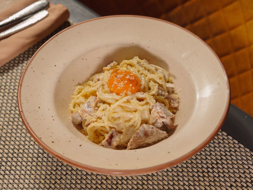Bowl of creamy carbonara pasta topped with black pepper and parmesan