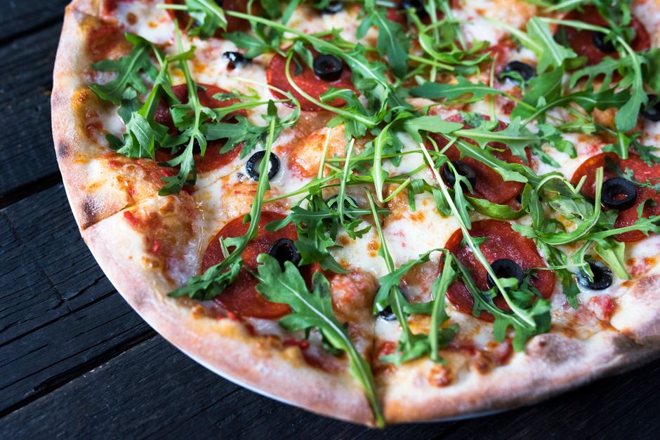 High angle of tasty pizza with black olive rings and fresh herb leaves on melted cheese