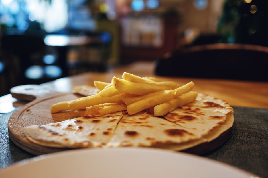 Close-up of a crispy quesadilla topped with golden french fries on a wooden board.