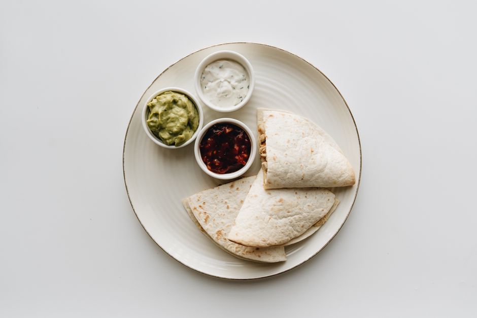 Sliced high-protein chicken quesadilla served with salsa and a side of sour cream
