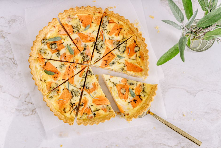 Top view of a delicious vegetable quiche sliced for serving with fresh herbs.